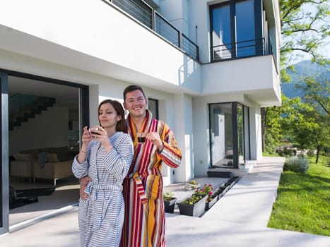 Young beautiful couple in bathrobes are enjoying morning coffee in front of their luxury home villa