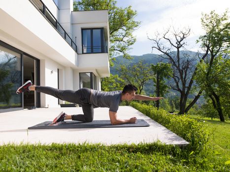 young handsome man doing morning yoga exercises in front of his luxury home villa