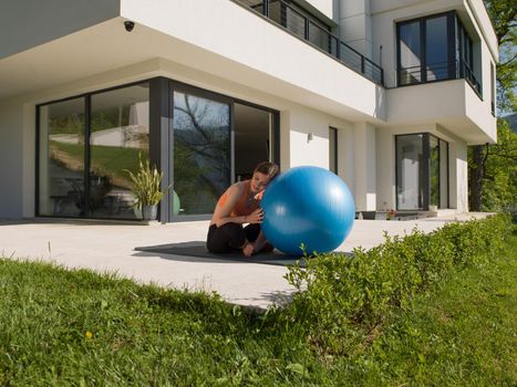 young beautiful woman doing exercise with pilates ball in front of her luxury home villa