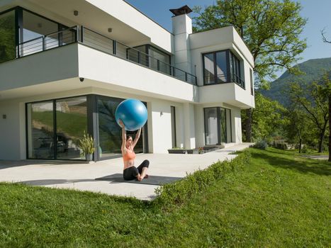 young beautiful woman doing exercise with pilates ball in front of her luxury home villa