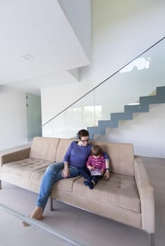 Beautiful young mother and her cute little daughter are using a tablet and smiling, sitting on sofa at home