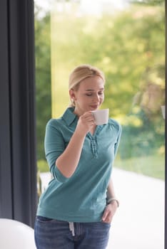 beautiful young woman drinking morning coffee by the window in her home