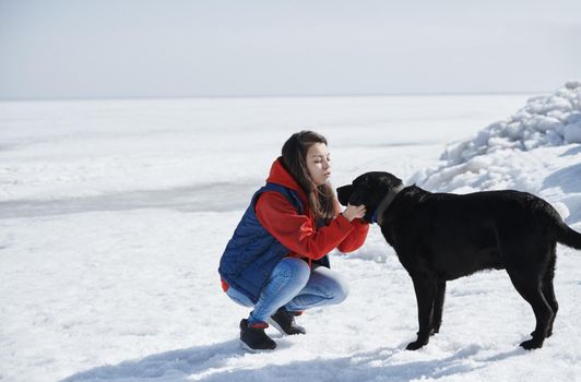 Young adult woman outdoors having fun with her black dog in icy landscape