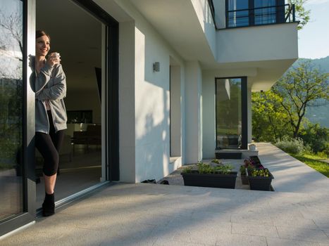 portrait of a young beautiful successful woman drinking coffee in the doorway of her luxury home villa