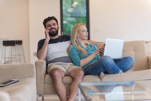 Young couple relaxes on the sofa in the luxury living room, using a laptop and remote control