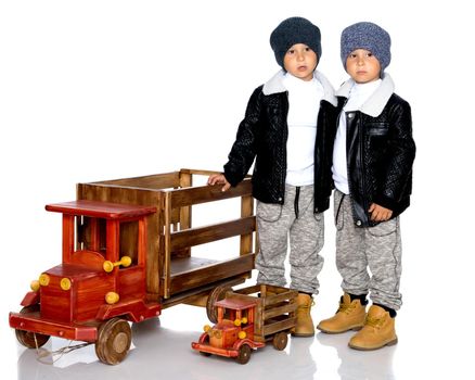 Two little boys play with wooden cars. In autumn jackets and hats. Isolated on white background.