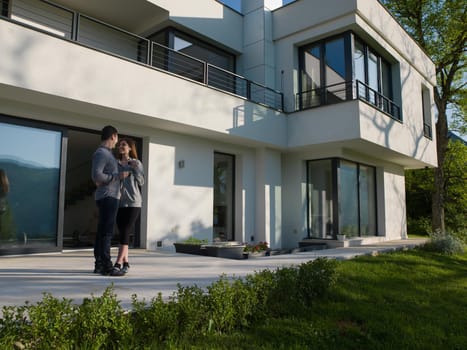 young beautiful handsome couple enjoying morning coffee in front of their luxury home villa