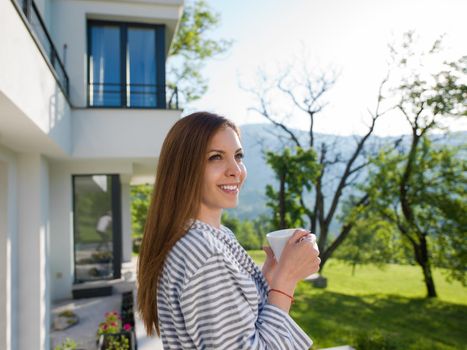 young beautiful woman in a bathrobe enjoying morning coffee in front of her luxury home villa