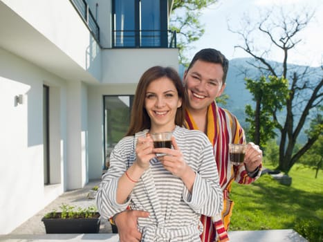 Young beautiful couple in bathrobes are enjoying morning coffee in front of their luxury home villa