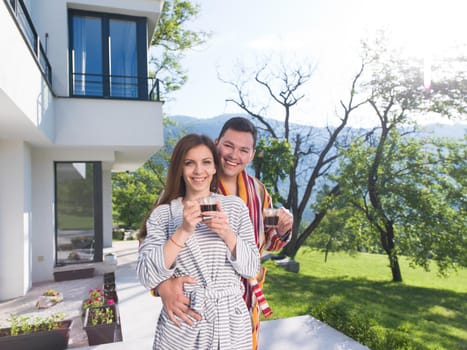 Young beautiful couple in bathrobes are enjoying morning coffee in front of their luxury home villa