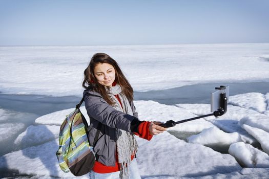 Female traveler outdoors at icy landscape using monopod to make selfie picture