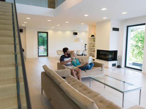 Young couple relaxes on the sofa in the luxury living room, using a laptop and remote control