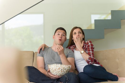 young handsome couple enjoying free time watching television with popcorn in their luxury home villa