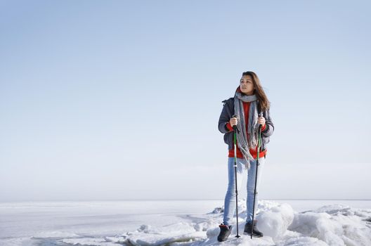 Young adult woman outdoors travelling in icy landscape with backpack and walking sticks 