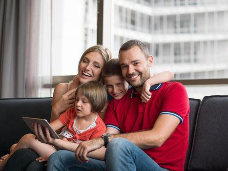 Happy Young Family Playing Together with tablet at home sitting on the sofa