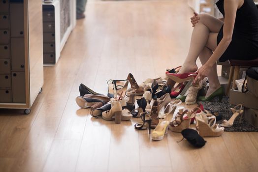 Hard choice. Close-up of young woman sitting in shoe store while different shoes laying near her
