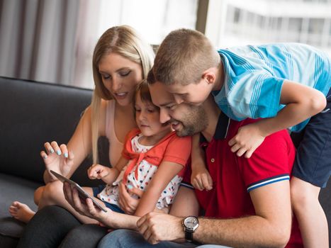 Happy Young Family Playing Together with tablet at home sitting on the sofa