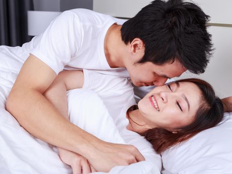 young man is kissing his beautiful smiling wife in cheek on bed