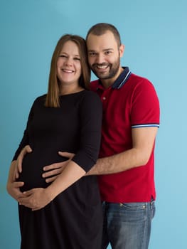 Portrait of a happy young couple,man holding his pregnant wife belly isolated over blue background