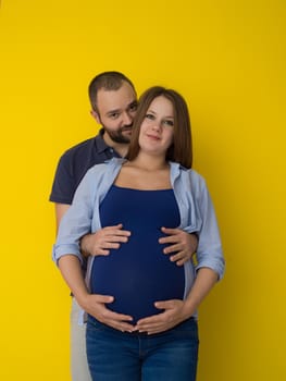 Portrait of a happy young couple,man holding his pregnant wife belly isolated over yellow background