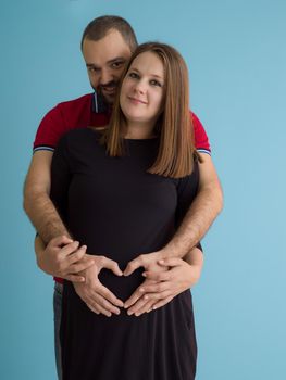 Portrait of a happy young couple,man holding his pregnant wife belly isolated over blue background