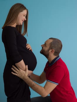 Portrait of a happy young couple,man holding his pregnant wife belly isolated over blue background