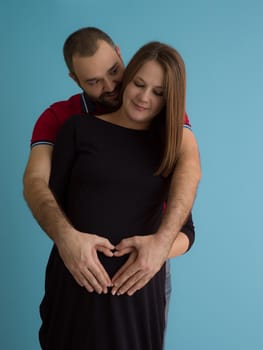 Portrait of a happy young couple,man holding his pregnant wife belly isolated over blue background