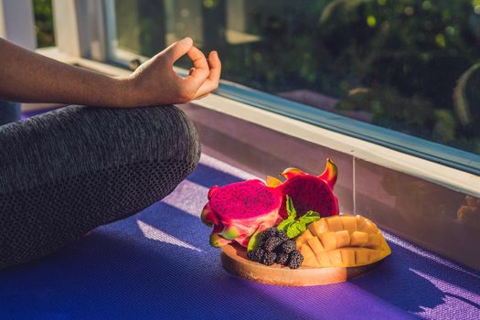 hand of a woman meditating in a yoga pose, sitting in lotus with fruits in front of her dragon fruit, mango and mulberry.