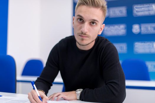 young male student writing notes in the classroom