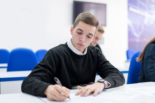young male student writing notes in the classroom