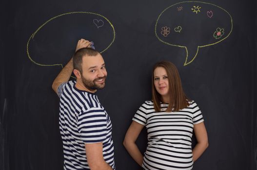 young pregnant couple thinking about names for their unborn baby and writing them on a black chalkboard