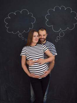 portrait of husband and pregnant wife posing against black chalk drawing board