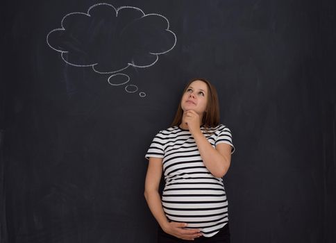 young pregnant woman thinking about names for her unborn baby to writing them on a black chalkboard