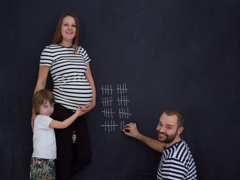 young pregnant couple with cute little daughter accounts week of pregnancy and writing them with chalk on blackboard