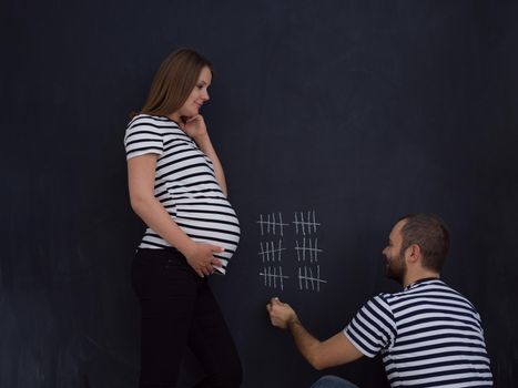 young pregnant couple accounts week of pregnancy and writing them with chalk on blackboard