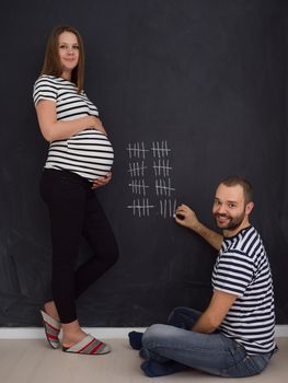 young pregnant couple accounts week of pregnancy and writing them with chalk on blackboard