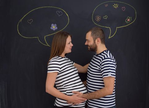 portrait of husband and pregnant wife posing against black chalk drawing board