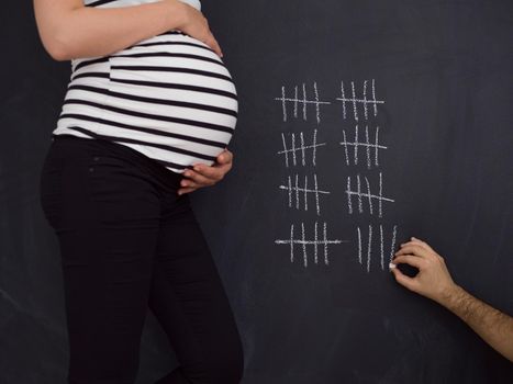 young pregnant couple accounts week of pregnancy and writing them with chalk on blackboard