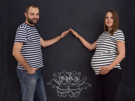 Conceptual photo of pregnant couple drawing their imaginations about the future life with children on chalk board