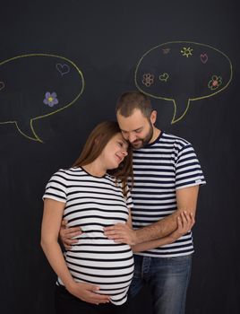 portrait of husband and pregnant wife posing against black chalk drawing board