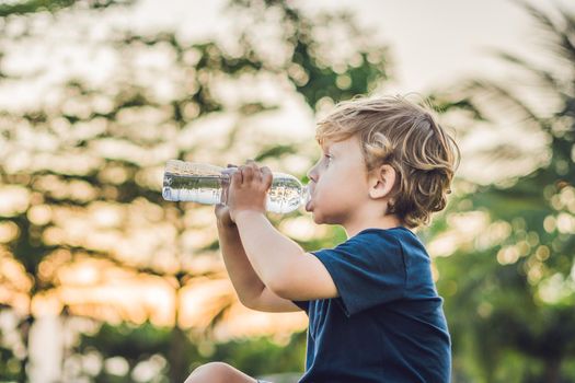 Kid drinking pure fresh water in nature at sunset.