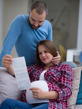 Young pregnant couple looking baby's ultrasound photo while relaxing on sofa at home