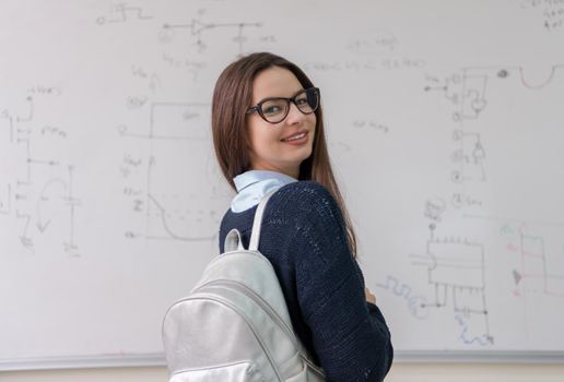 portrait of a young beautiful female student standing in front of white chalkboard and looking at the camera