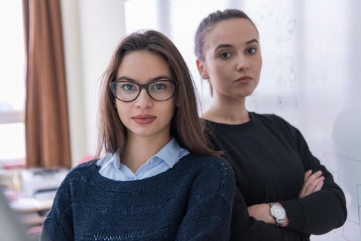 portrait of two young female students standing in front of a white chalkboard and looking at the camera