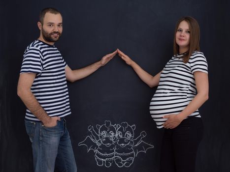 Conceptual photo of pregnant couple drawing their imaginations about the future life with children on chalk board