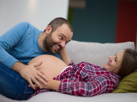 Happy future dad listening the belly of his pregnant wife while relaxing on sofa at home