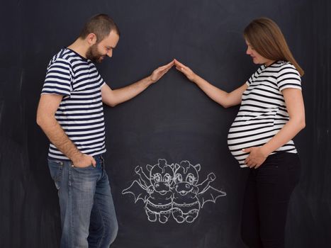 Conceptual photo of pregnant couple drawing their imaginations about the future life with children on chalk board