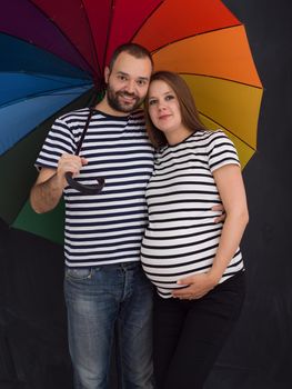 portrait of husband and pregnant wife posing with colorful umbrella in front of black chalk drawing board