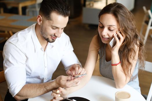 Young woman talking by smartphone and sitting with man using hotspot at cafe. Concept of happy couple and relationship, modern technology and internet.