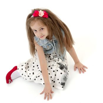 Beautiful little girl is sitting on the floor in the studio. The concept of a happy childhood, beauty and fashion. Isolated on white background.